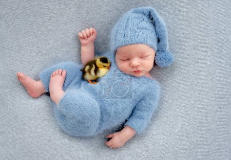 Foto de Niño recién nacido durmiendo con una chica patita. Niño adorable niño que duerme usando sombrero de punto y traje - Imagen libre de derechos