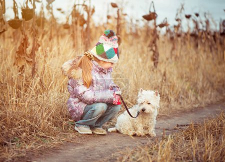 Téléchargez les photos : Petite fille avec son chien race White Terrier marche dans un champ en automne - en image libre de droit