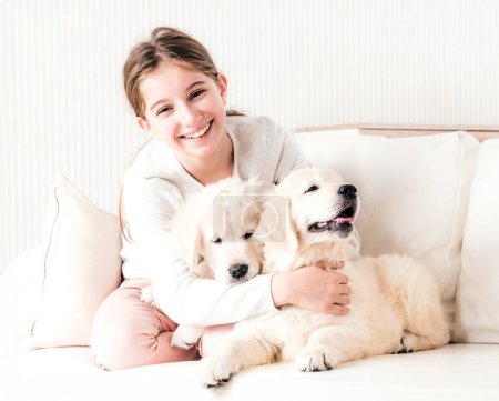 Foto de Sonriente chica sentarse abrazando lindo cachorros en sofá - Imagen libre de derechos