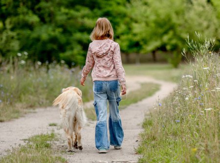 Photo for Preteen girl with golden retriever dog walking at nature. Cute child kid with purebred pet doggy labrador in park at summer - Royalty Free Image