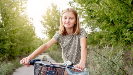 Photo for Cute preteen girl with bycicle outdoors looking at camera and smiling. Pretty child with bike at city street at summer park - Royalty Free Image