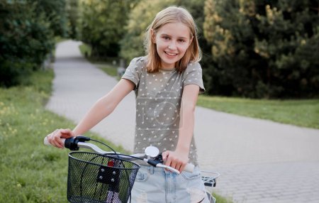 Foto de Linda chica preadolescente con bicicleta al aire libre mirando a la cámara y sonriendo. Niño bonito con bicicleta en la calle de la ciudad en el parque de verano - Imagen libre de derechos