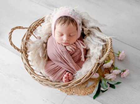 Entzückendes neugeborenes Mädchen liegt im Korb mit Pfingstrosenblumen Dekoration Porträt. Niedliches Säugling Kind in Stoff gewickelt schlafen