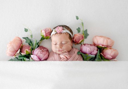Téléchargez les photos : Adorable petite fille nouveau-née dormant dans des fleurs de pivoine. Enfant bébé mignon dormant dans des plantes roses portant une couronne - en image libre de droit