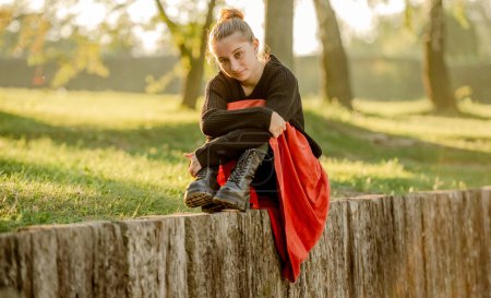 Téléchargez les photos : Belle adolescente en jupe rouge assise dans le parc en plein air à la nature. Jolie adolescente modèle en vêtements à la mode à la rue - en image libre de droit