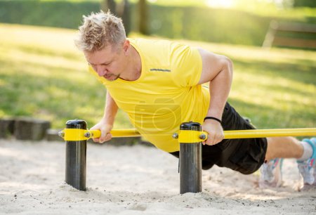Photo for Man doing push ups with horizontal bar outdoors in park for healthy wellbeing. Sportsman guy making strong workout for muscle - Royalty Free Image