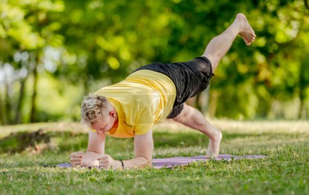 Photo for Man standing in plank position and practicing yoga outdoors at summer. Guy doing pilates workout for stretching muscles and abs stretght - Royalty Free Image