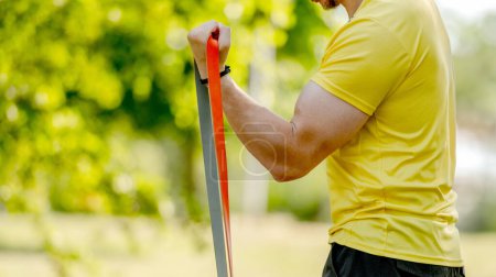 Photo for Man excercising with elastic rubber band outdoors making arm workout. Guy making fitness with sport equipment - Royalty Free Image