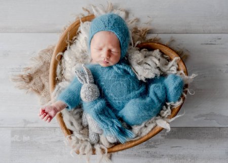 Photo for Adorable newborn baby boy sleeping holding knitted bunny toy in heart shape basket studio portrait. Cute infant child kid napping - Royalty Free Image