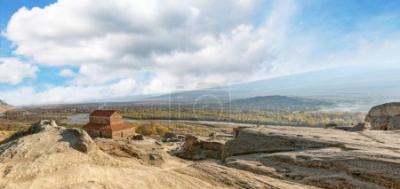 Téléchargez les photos : Vue panoramique de la ville rocheuse d'Uplistsikhe surplombant la ville lointaine et la rivière - en image libre de droit