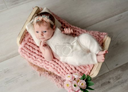 Foto de Adorable niña recién nacida acostada en una cama pequeña sobre un retrato de piel. Niño lindo bebé envuelto en tela descansando en la habitación con luz del día - Imagen libre de derechos