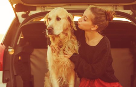 Photo for Beautiful girl with golden retriever dog sitting in car trunk and smiling. Pretty teenager hugging purebred pet doggy in vehicle at autumn nature - Royalty Free Image