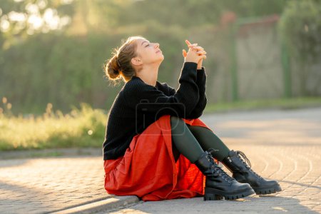 Photo for Beautiful teenager girl in red skirt sitting outdoors at street. Pretty teen model posing in trendy clothes - Royalty Free Image