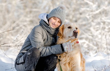 Photo for Teenage Girl And Golden Retriever Sit Together In Snow-Covered Forest During Winter - Royalty Free Image