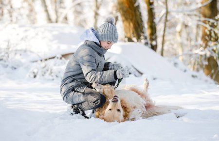 Foto de Adolescente chica juega con Golden Retriever en el bosque nevado, sentado con perro - Imagen libre de derechos