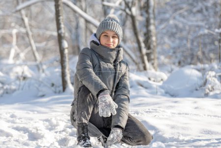 Téléchargez les photos : Adolescente s'assoit et pose pour une photo dans une forêt enneigée en hiver - en image libre de droit