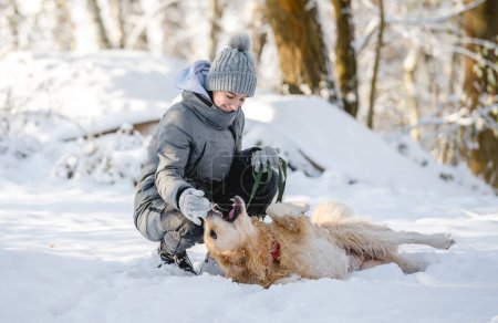 Téléchargez les photos : Adolescente joue avec Golden Retriever dans la forêt enneigée, Assis avec chien - en image libre de droit