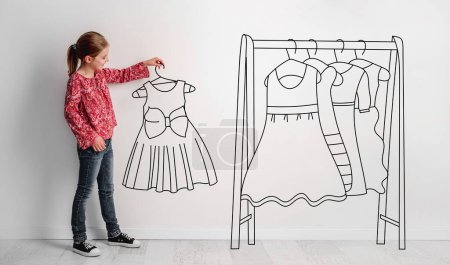 Photo for Photo Of Little Girl Holding Hand-Drawn Dress, With Illustrated Hanger And Dresses Nearby, Combines Photography And Illustration On The Theme Of ChildrenS Fashion - Royalty Free Image