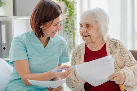 Photo for Smiling Nurse Gives Elderly Woman Documents To Read In DoctorS Office - Royalty Free Image