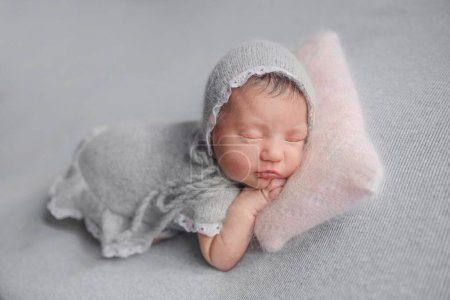 Téléchargez les photos : Fille nouveau-né dort en robe grise pendant la séance photo de bébé en studio - en image libre de droit