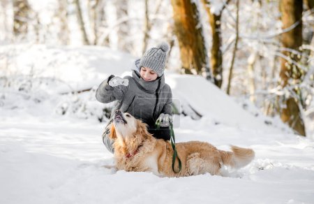 Foto de Adolescente chica juega con Golden Retriever en el bosque nevado, sentado con perro - Imagen libre de derechos