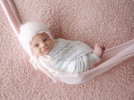 Téléchargez les photos : Le nouveau-né, emmailloté dans une couverture, dort dans un hamac pendant une séance de photo avec un sourire - en image libre de droit