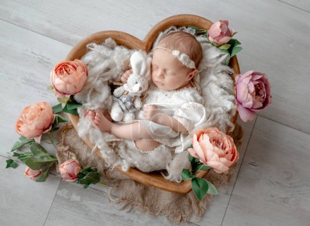 Téléchargez les photos : Le nouveau-né dort dans un bol en bois en forme de coeur parmi les fleurs pendant la séance photo en studio - en image libre de droit