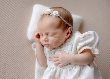 Téléchargez les photos : Bébé fille en robe dort sur fond de tissu beige pendant la séance photo nouveau-né en studio - en image libre de droit