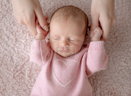 Téléchargez les photos : Bébé fille en tenue rose dort pendant que maman la tient pendant la séance photo du nouveau-né en studio - en image libre de droit