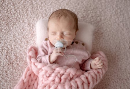 Téléchargez les photos : Bébé fille en tenue rose dort avec sucette pendant la séance photo nouveau-né en studio - en image libre de droit