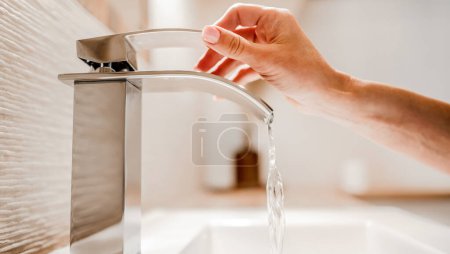 Photo for Girl hand open water from steel faucet in bathroom. Woman using silver tap at home for cleaning and hygiene - Royalty Free Image