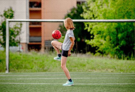 Photo for Pretty child girl kicking football ball at socket field. Cute female kid playing active game - Royalty Free Image