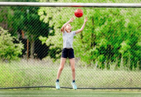 Foto de Niña bonita atrapando pelota de fútbol defendiendo gol. Lindo niño femenino en el campo de fútbol jugando - Imagen libre de derechos