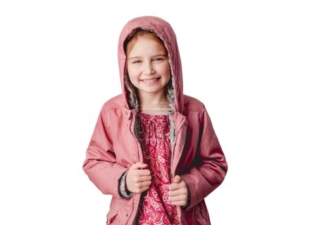 Téléchargez les photos : Petite fille en veste rose souriant à la caméra tout en se tenant à l'intérieur sur fond de mur blanc - en image libre de droit