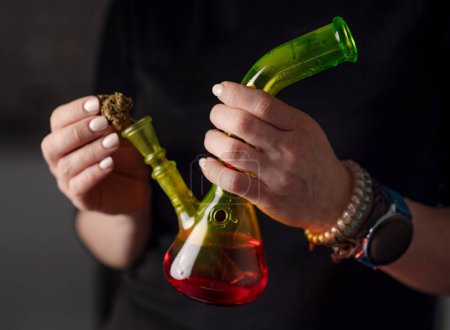Téléchargez les photos : Femme remplit Bong avec des feuilles de cannabis, détail de la main féminine préparant la marijuana pour l'utilisation - en image libre de droit