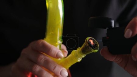 Photo for Burning And Smoking Hemp Leaves From A Bong, Flame Close-Up, With Female Hands - Royalty Free Image