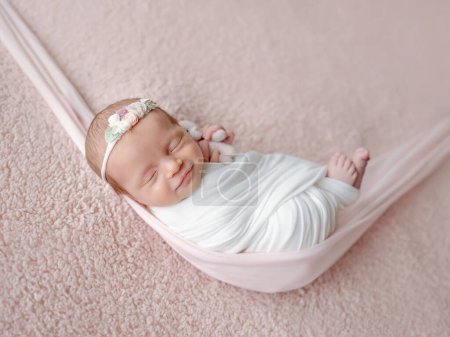 Neugeborenes Baby, in eine Decke gewickelt, schläft in einer Hängematte während einer Fotosession mit einem Lächeln