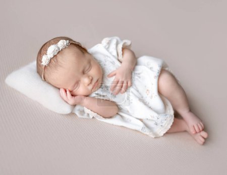 Foto de Bebé niña en vestido duerme sobre fondo de tela beige durante la sesión de fotos del recién nacido en el estudio - Imagen libre de derechos