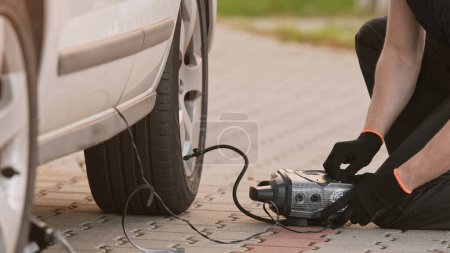 Photo for Man Inflates Tire Using Portable Pump As Driver - Royalty Free Image