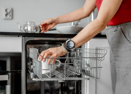 Junge Frau holt saubere Gerichte aus Spülmaschine in Nahaufnahme