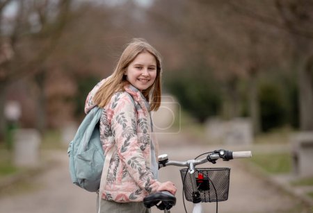 Photo for Smiling Girl Holds Bicycle In Spring With Blurred Park Background - Royalty Free Image