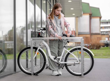 Chica sujeta la bicicleta cerca de estacionamiento de bicicletas de supermercado en primavera