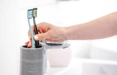 Photo for GirlS Hand Places Two Toothbrushes In Cup, Marking Start Of CoupleS Life Together - Royalty Free Image