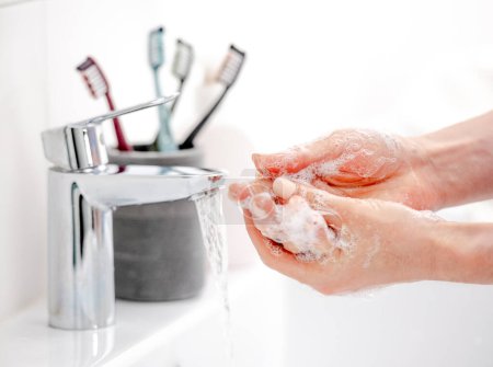 Téléchargez les photos : Fille se lave les mains avec du savon liquide dans la baignoire vierge - en image libre de droit