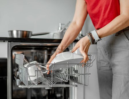Photo for Young Woman Takes Out Clean Dishes From Dishwasher In Close-Up Shot - Royalty Free Image