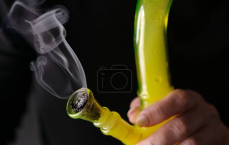 Photo for Woman Smokes Marijuana With Bong In Close-Up, Representing Lifestyle Concepts And Worldwide Legalization Of Marijuana - Royalty Free Image