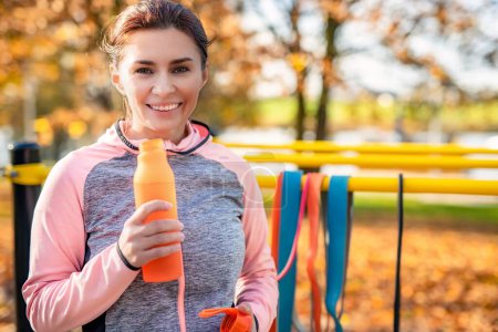 Téléchargez les photos : Fitness fille avec bouteille d'eau après l'exercice dans le parc d'automne à l'extérieur. Jeune femme et portrait sportif d'hydratation à l'automne - en image libre de droit