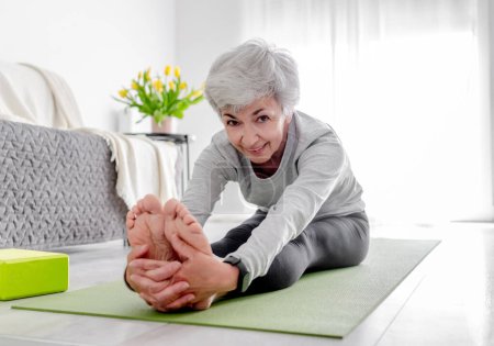 Style de vie sportif à la retraite, une douce femme aux cheveux gris exerce sur le plancher du salon