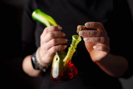 Téléchargez les photos : Femme remplit Bong avec des feuilles de cannabis, détail de la main féminine préparant la marijuana pour l'utilisation - en image libre de droit