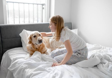 Foto de Pequeña chica juega con Golden Retriever perro en la cama - Imagen libre de derechos